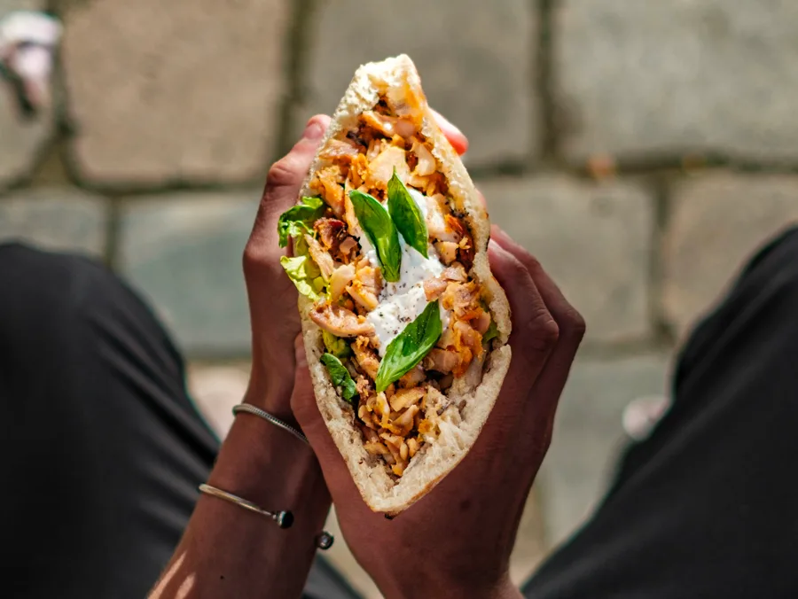 Kebab artisanal Frau tenu à deux mains, garni de poulet et basilic
